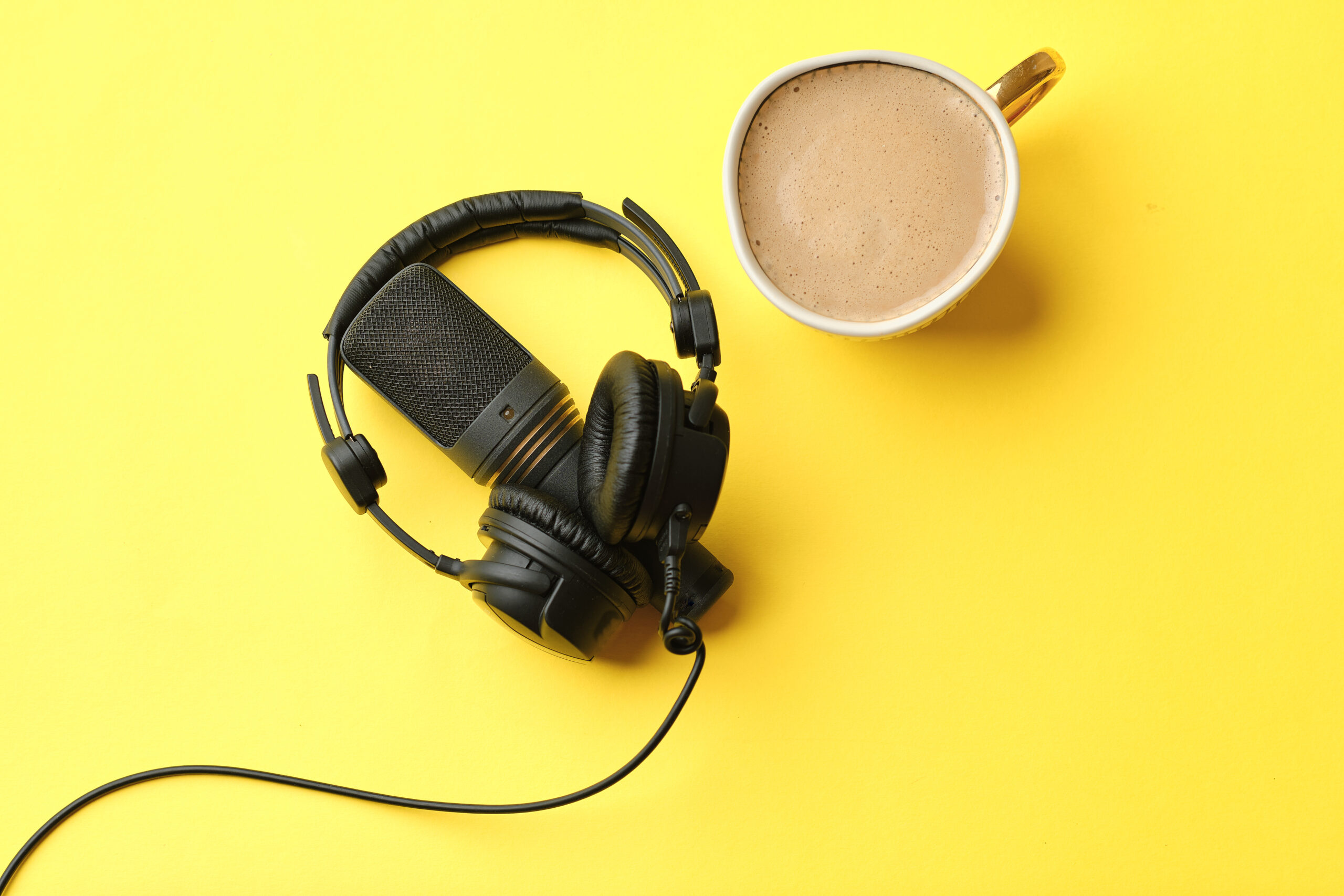 Flat lay composition with Microphone for podcasts and black studio headphones on yellow background with coffee, learning online education concept.