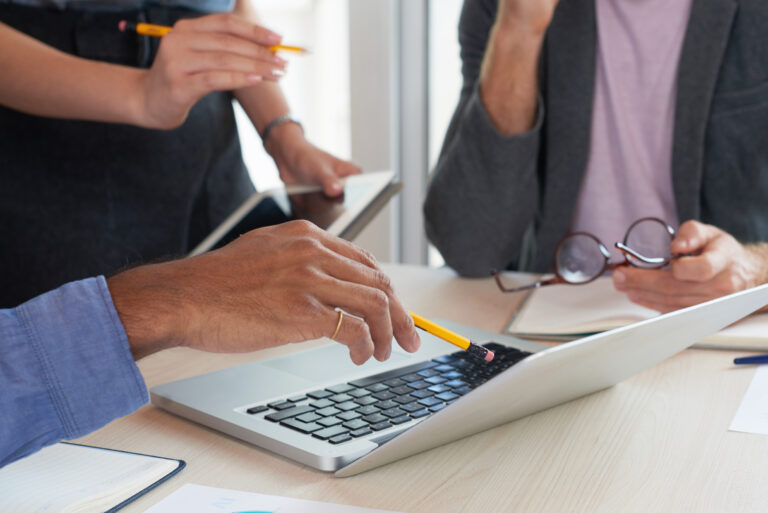 Close-up of businessman pointing at laptop and discussing some facts with his colleagues at meeting